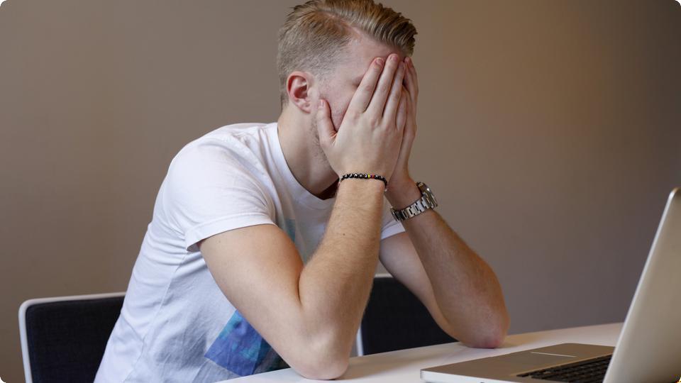 Kille sitter  med händerna framför ansiktet vid sin dator, han verkar stressad.